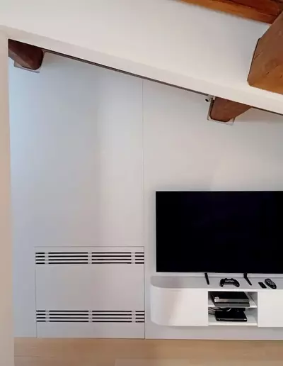 Boiserie su misura con mobile TV sospeso e griglie di ventilazione integrate in ambiente mansardato a Firenze.