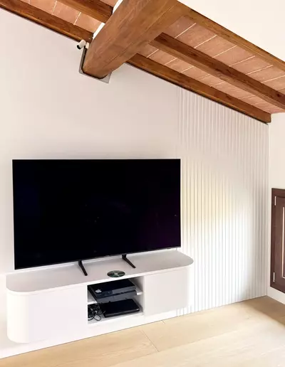 Mobile TV sospeso su misura con boiserie bianca e soffitto in legno a vista – falegnameria artigianale Firenze.